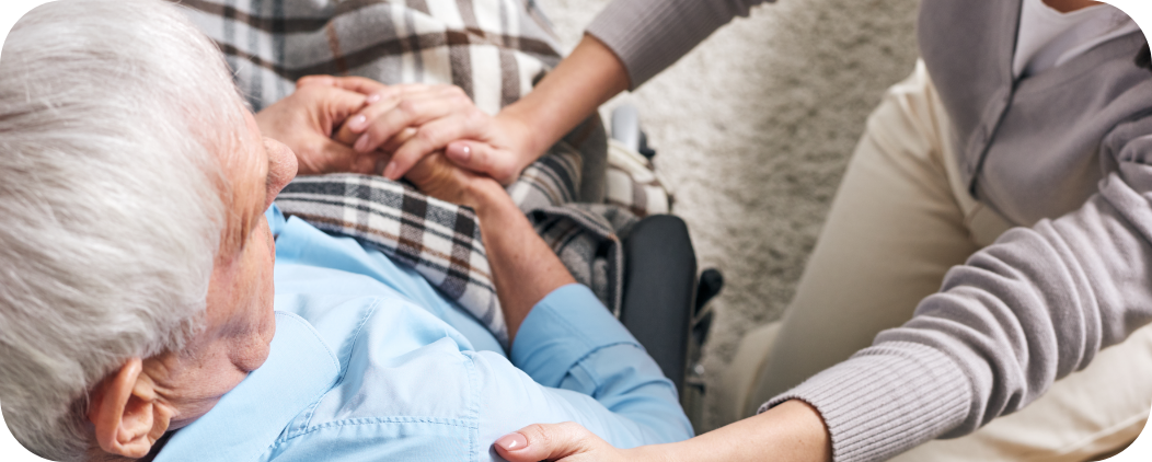 Une auxiliaire de vie de l'association Le Connétable à Dinan tient chaleureusement la main d'un senior en fauteuil roulant, symbolisant le soutien humain et le réconfort apportés par l'aide à domicile - Association Le Connétable à Dinan